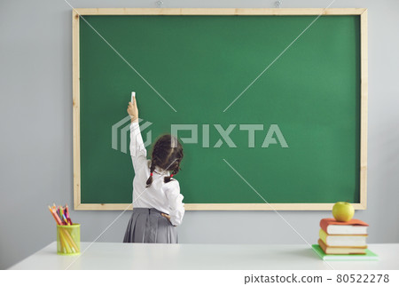 Back to school. Little schoolgirl writes on the school blackboard with chalk in the classroom. 80522278