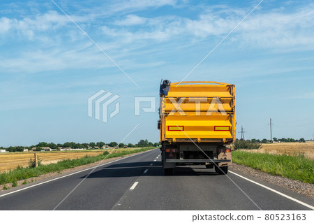 Big modern yellow grain hopper cargo truck driving on highway to silo granary storage unloading aginst clear blue sky on bright summer day. Cereal harvesting and shipping industrial season 80523163