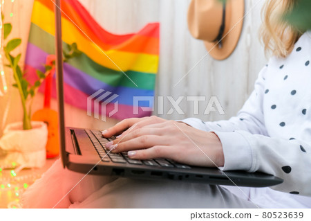 Young millennial hippie woman sitting on balcony using laptop. LGBTQ rainbow flag on background. Online education tuition. Work from home. Modern office. 80523639