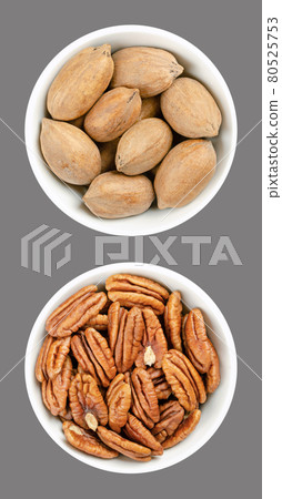 Pecan nuts, shelled and unshelled, in white bowls, over gray. Whole pecans and pecan halves, seeds and nuts of Carya illinoinensis, a popular snack. Close-up, from above, isolated, macro food photo. 80525753