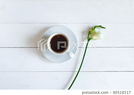 coffee cup with saucer and white freesia flower on white wood background. Top view, flat lay. Place for your text and product. Aroma and good morning concept. 80528517