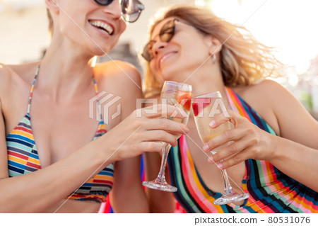 Two young adult girlfriends enjoy have fun celebrate happy moments drinking and cheers champagne wine glasses at ocean sea beach summer vacation. LGBT bisexual lifestyle life and travel concept 80531076