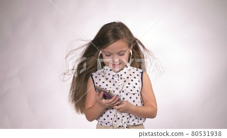 Child with headphones dancing at studio background. Girl listens to music on smartphone. Beautiful cute happy little girl listens to music. Child with headphones dancing at studio background. Girl listens to music on smartphone. Beautiful cute happy little girl listens to music. 80531938