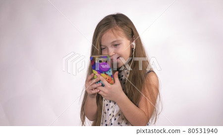 Child with headphones dancing at studio background. Girl listens to music on smartphone. Beautiful cute happy little girl listens to music. Child with headphones dancing at studio background. Girl listens to music on smartphone. Beautiful cute happy little girl listens to music. 80531940