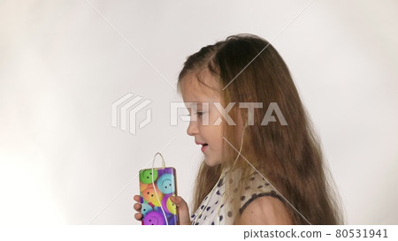 Child with headphones dancing at studio background. Girl listens to music on smartphone. Beautiful cute happy little girl listens to music. Child with headphones dancing at studio background. Girl listens to music on smartphone. Beautiful cute happy little girl listens to music. 80531941