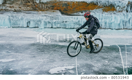 Man is riding bicycle near ice grotto. Rock with ice caves icicl Man is riding bicycle near ice grotto. Rock with ice caves icicl 80531943