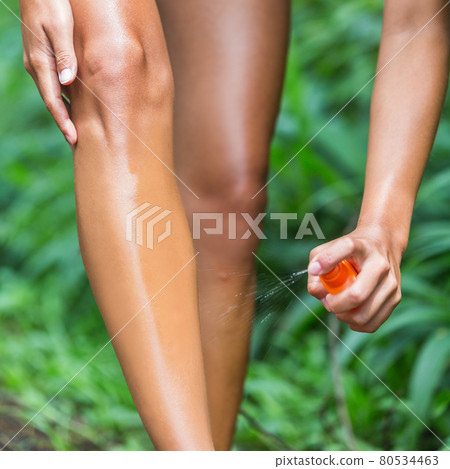 Woman spraying mosquito repellent on leg skin. Woman using Insect repellent bug spray bottle on legs, body and clothing outdoor in nature forest. Prevention for zika virus affecting tropical areas. 80534463