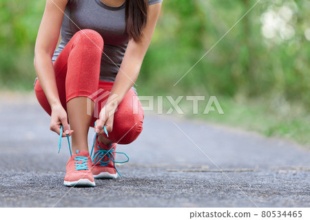 Running shoes - closeup of woman tying shoe laces. Female sport fitness runner getting ready for jogging outdoors on forest path in summer season. Running shoes - closeup of woman tying shoe laces. Female sport fitness runner getting ready for jogging outdoors on forest path in summer season. 80534465