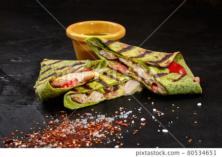 Sliced burrito in spinach tortilla with chicken on black surface Sliced burrito in spinach tortilla with chicken on black surface 80534651