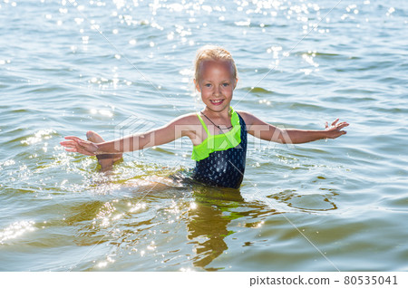 Little girl is laughing and swimming at sea on a sunny day Little girl is laughing and swimming at sea on a sunny day 80535041