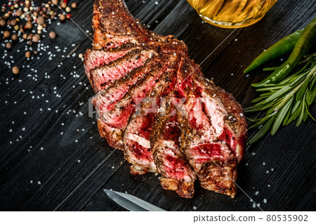Barbecue dry aged rib of beef with spice, vegetables and a glass of light beer close-up on black wooden background Barbecue dry aged rib of beef with spice, vegetables and a glass of light beer close-up on black wooden background 80535902