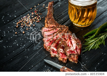 Barbecue dry aged rib of beef with spice, vegetables and a glass of light beer close-up on black wooden background 80535904
