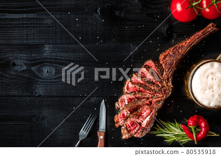 Barbecue dry aged rib of beef with spice, vegetables and a glass of light beer close-up on black wooden background 80535918