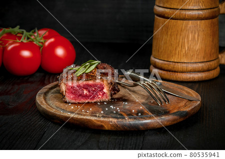 Grilled steak seasoned with spices and fresh herbs served on a wooden board with wooden mug of beer and fresh tomato Grilled steak seasoned with spices and fresh herbs served on a wooden board with wooden mug of beer and fresh tomato 80535941