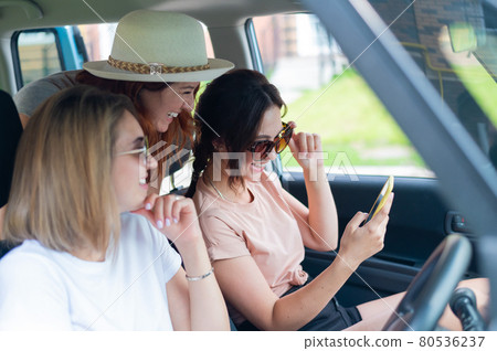 Three happy girlfriends go on a trip. Women are driving in a car and taking a selfie on a mobile phone Three happy girlfriends go on a trip. Women are driving in a car and taking a selfie on a mobile phone 80536237