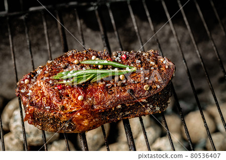 Hot spicy steak grilling on a summer barbecue over the hot coals garnished decorated with a branch of rosemary Hot spicy steak grilling on a summer barbecue over the hot coals garnished decorated with a branch of rosemary 80536407