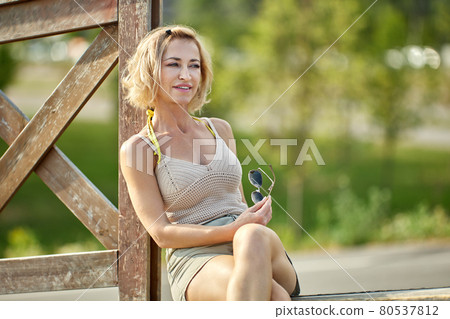 Happy attractive middle-aged woman sits outdoors in park. Happy attractive middle-aged woman sits outdoors in park. 80537812