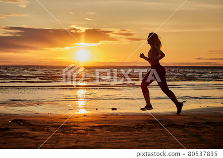 Healthy woman runs outdoors during sunset near shore. Healthy woman runs outdoors during sunset near shore. 80537835