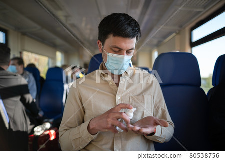 New normal commuting with face mask and hand sanitizer. Travel safely on public transport. Passenger with protective mask disinfects hands in a railway train. Travel during covid 19, personal protect New normal commuting with face mask and hand sanitizer. Travel safely on public transport. Passenger with protective mask disinfects hands in a railway train. Travel during covid 19, personal protect 80538756