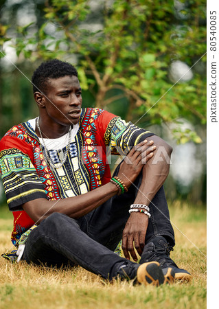 An African man in South African national clothes, a black young man resting in a park in national clothes. An African man in South African national clothes, a black young man resting in a park in national clothes. 80540085