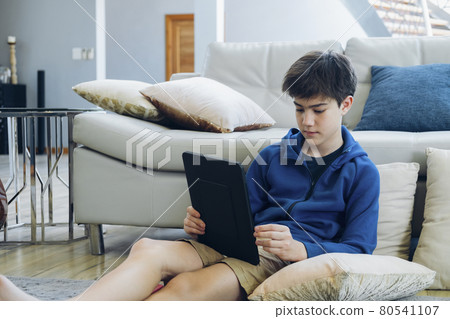 The boy using tablet computer while sitting on sofa at home. The boy using tablet computer while sitting on sofa at home. 80541107