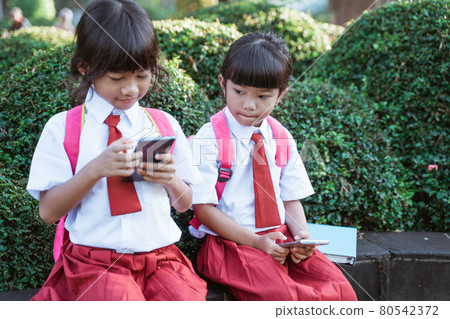 asian primary student using mobile phone in school park asian primary student using mobile phone in school park 80542372