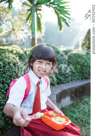 kid school student enjoying eating her meal in lunch box during school break kid school student enjoying eating her meal in lunch box during school break 80542402