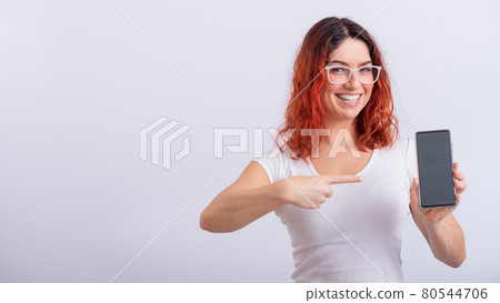 A Caucasian woman points to a smartphone with a blank screen on a white background 80544706
