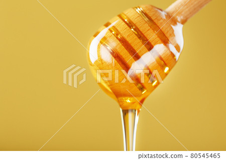 Golden honey trickles from a wooden honey dipper on a yellow background Golden honey trickles from a wooden honey dipper on a yellow background 80545465