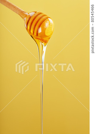 Honey drips in a thin stream from a honey dipper on a yellow background. Honey drips in a thin stream from a honey dipper on a yellow background. 80545466