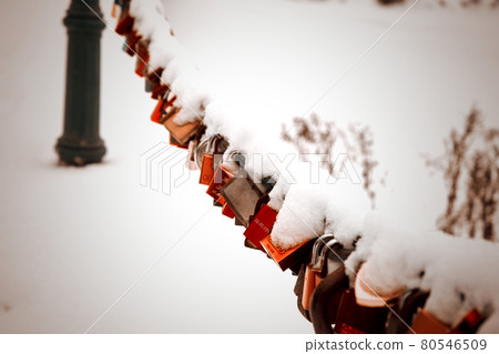 Love locks covered by snow on a chain in front of a bridge over a moat Love locks covered by snow on a chain in front of a bridge over a moat 80546509