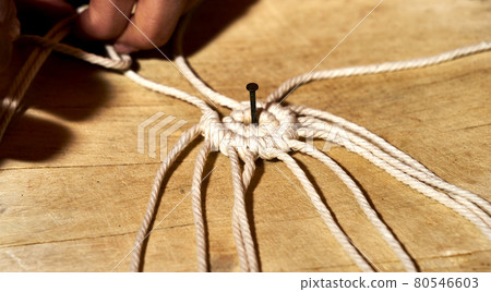 First knots to make a macrame coaster from a rope on a plate of wood First knots to make a macrame coaster from a rope on a plate of wood 80546603