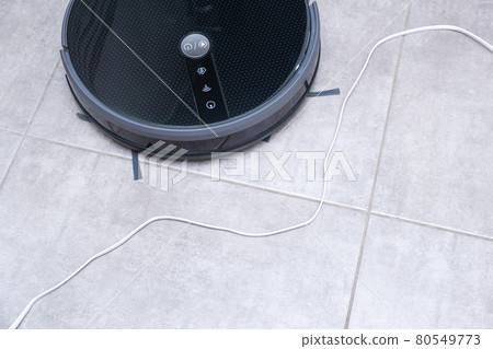 Robot vacuum cleaner on a brown floor. Obstacle in the form of wires. The robot vacuum cleaner is entangled in the wires. Robot vacuum cleaner on a brown floor. Obstacle in the form of wires. The robot vacuum cleaner is entangled in the wires. 80549773