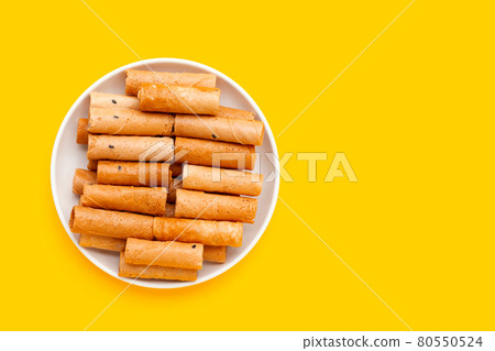 Thai crispy coconut rolls in white plate on yellow background. Thai crispy coconut rolls in white plate on yellow background. 80550524