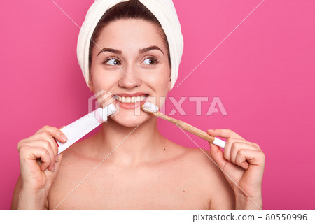 Woman dreaming in bathroom, attractive female with toothbrush and toothpaste in hands posing isolated over rosy background, looking aside, wrapped white towel, morning procedures in bathroom. Woman dreaming in bathroom, attractive female with toothbrush and toothpaste in hands posing isolated over rosy background, looking aside, wrapped white towel, morning procedures in bathroom. 80550996