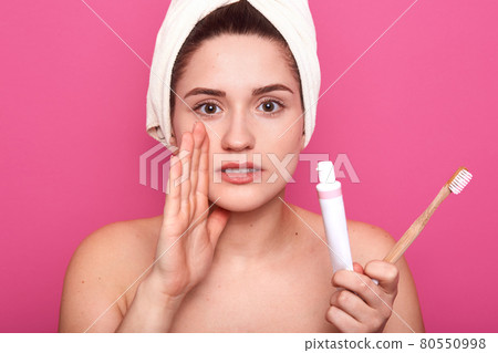 Attractive caucasian woman isolated on pink studio background, young female ready to brush her teeth, being photogrephed with naked shoulders and with white towel on head, keeps hand near mouth. Attractive caucasian woman isolated on pink studio background, young female ready to brush her teeth, being photogrephed with naked shoulders and with white towel on head, keeps hand near mouth. 80550998