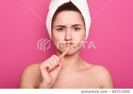 Close up portrait of attractive caucasian woman with dark hair posing isolated over pink background, femaklw with bare shouldersand white towel on head, lady looking at camera, brushing teeth. Close up portrait of attractive caucasian woman with dark hair posing isolated over pink background, femaklw with bare shouldersand white towel on head, lady looking at camera, brushing teeth. 80551000
