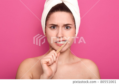 Close up portrait of naked emotional woman doing hygiene procedures with dissatisfaction, holding wooden toothbrush in her cavity, covering her head with towel, feeling unwell. Dental care concept. Close up portrait of naked emotional woman doing hygiene procedures with dissatisfaction, holding wooden toothbrush in her cavity, covering her head with towel, feeling unwell. Dental care concept. 80551001