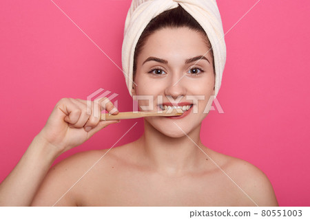 Happy adorable woman with white towel on her head doing morning procedures in bathroom, lady with fresh clean skin looks at camera while brushing teeth. Happy adorable woman with white towel on her head doing morning procedures in bathroom, lady with fresh clean skin looks at camera while brushing teeth. 80551003