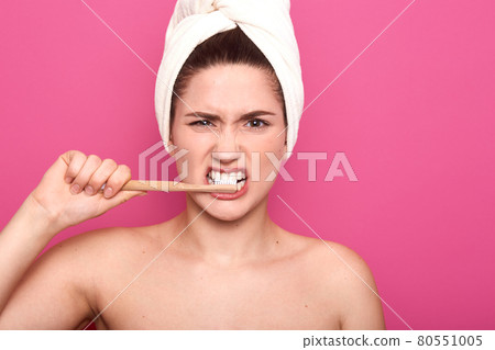 Closeup portrait of funny lady posing naked, holding her dental equipment in one hand, brushing her teeth carefully, covering her hair with white towel, standing isolated over pink background. 80551005