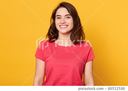 Image of attractive woman with dark hair being very glad, looking with broad smile showing her perfect teeth, excited female wearing red casual t shirt, posing isolated over yellow background. Image of attractive woman with dark hair being very glad, looking with broad smile showing her perfect teeth, excited female wearing red casual t shirt, posing isolated over yellow background. 80552580