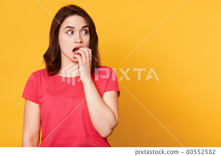 Half length front portrait of beautiful female isolated on yellow studio backgroud. Young emotional surprised woman standing with open mouth and covering it with fist. Human emotions concept. Half length front portrait of beautiful female isolated on yellow studio backgroud. Young emotional surprised woman standing with open mouth and covering it with fist. Human emotions concept. 80552582