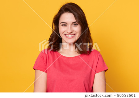 Picture of Caucasian brunette woman posing isolated over yellow background, dark haired lady looks smiling directly at camera, looking happy, lady wearing red t shirt. People emotions concept. Picture of Caucasian brunette woman posing isolated over yellow background, dark haired lady looks smiling directly at camera, looking happy, lady wearing red t shirt. People emotions concept. 80552601