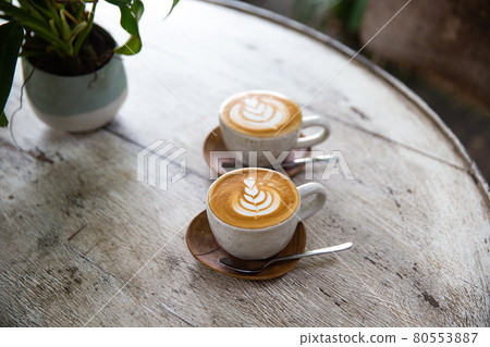Two cups of cappuccino with latte art on saucer with spoons white wooden background Two cups of cappuccino with latte art on saucer with spoons white wooden background 80553887