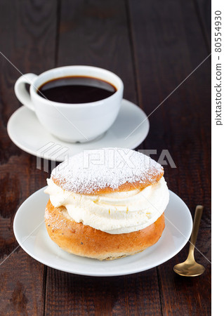 Traditional Swedish dessert Semla or Shrove bun, with almond paste and whipped cream filling, served with cup of coffee, vertical 80554930