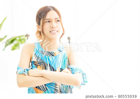 A young woman in a one-piece, laughing with her arms crossed by the window in a bright room A young woman in a one-piece, laughing with her arms crossed by the window in a bright room 80555039
