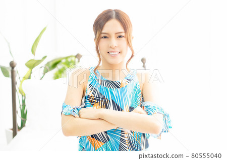 A young woman in a one-piece, laughing with her arms crossed by the window in a bright room A young woman in a one-piece, laughing with her arms crossed by the window in a bright room 80555040