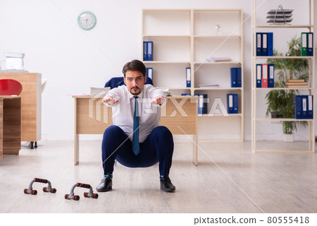 Young male employee doing sport exercises during break 80555418