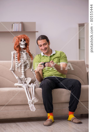 Young man sitting on the sofa with female skeleton Young man sitting on the sofa with female skeleton 80555444