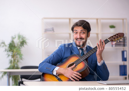 Young male employee playing guitar at workplace Young male employee playing guitar at workplace 80555452